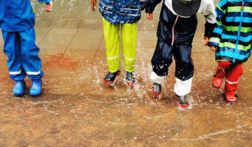 Barn plaskar i vattnet med regnkläder på.