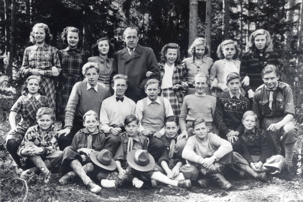 Läraren Bernhard Bengtsson med elever i klass 7 i Hjälmsta skola. Fotograferat utomhus, flera av pojkarna har scoutkläder, St Georgdagen?.  Övre raden fr v okänd, Margareta Tillborg, Gun Lindersson, Bernhard Bengtsson,  nr 5-8 okända.  Mellanraden nr 2 ? Eriksson, nr 5 Lennart Karlsson, nr 6 Kalle Söderström.  Sittande nr 1 ? Sandin