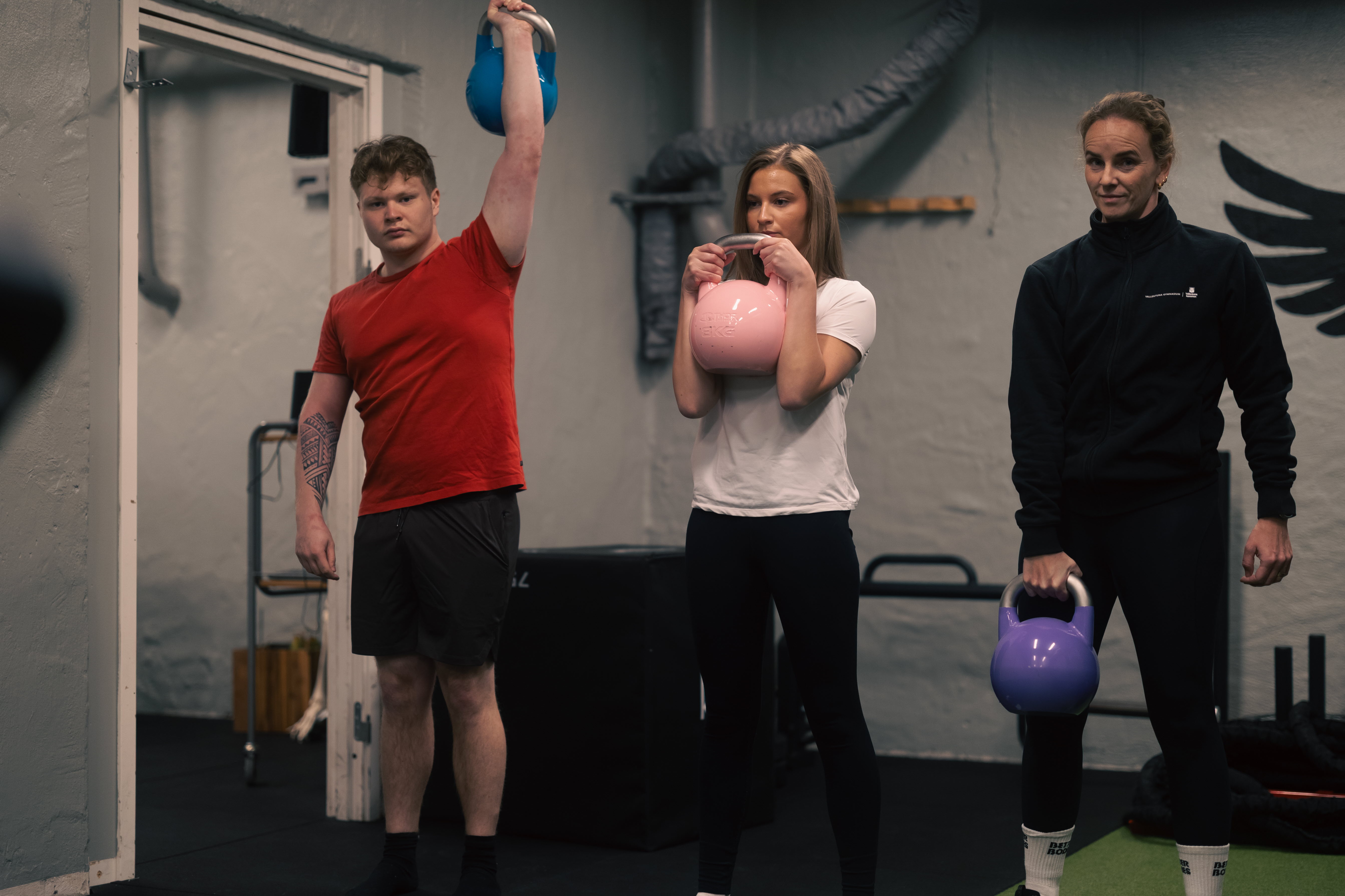 Två elever tillsamman med lärare står bredvid varandra med varsin kettlebell i handen.