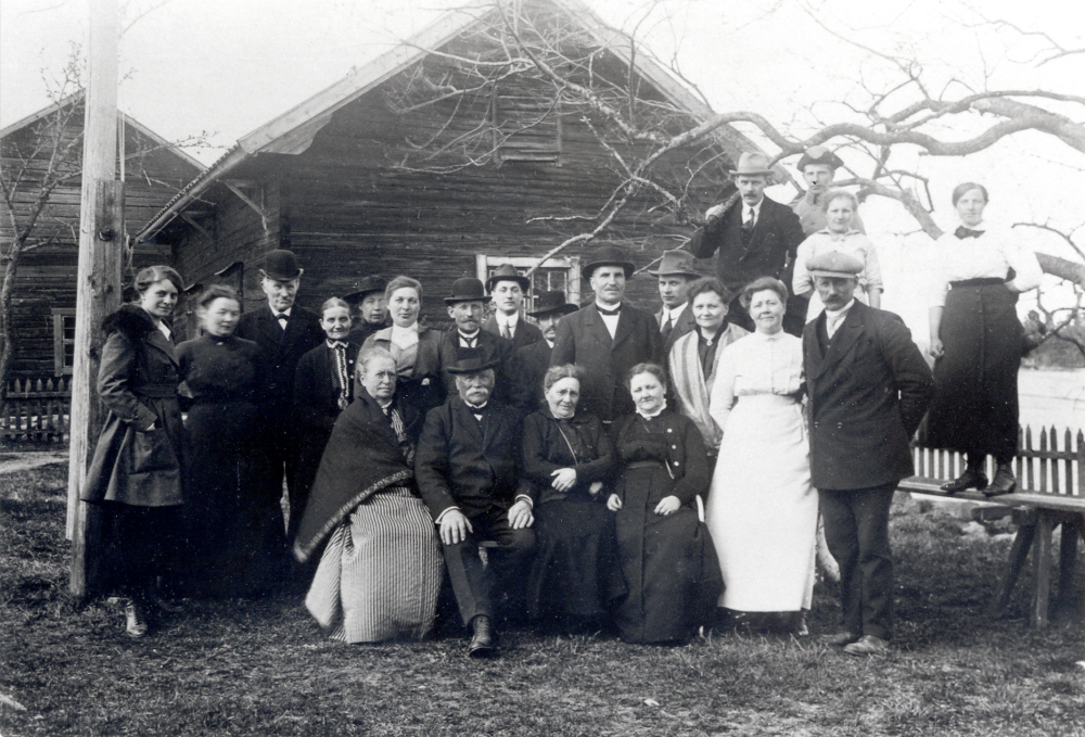 Samling utanför Lidberga gård, vid Väsby,  i Össeby-Garn.  Det äldre paret som sitter t v är fru och herr Wessman.  I bakre raden står som nr 4 och 5 fr v Ina och Sofie Wessman.  Paret i främre raden t h, kvinnan i vit klänning är Frida Singman och  bredvid henne Karl Singman.  Mannen i ljus hatt på bänken bakom Frida är Edvard Johansson, senare handlare i Karlborg, Angarn.  Kopia av vykort poststämplat 1918