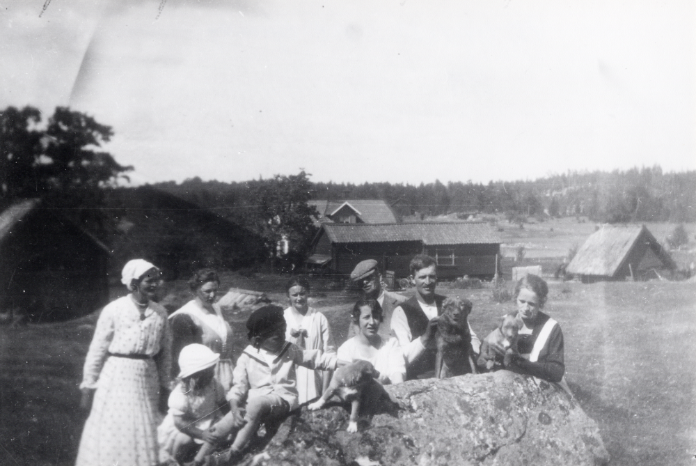 På logslätten vid Björky.  I bakgrunden gårdens ekonomibyggnader.  Huset längst t h har halmtak.  Personer fr v okänd, okänd, Elna Gustavsson, Allan Gustavsson?, okänd, Hildur Eriksson med en hundvalp framför sig, okänd man med keps, Karl Gustavsson med en hund, samt Ester Jansson med en hundvalp
