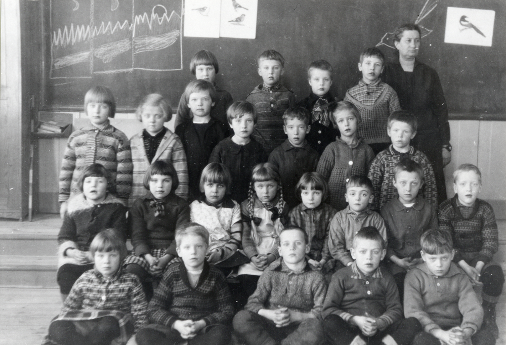 Hjälmsta skola. Lärarinnan Anna Gauffin tillsammans med skolbarnen inne i skolsalen. Enligt notering på kortets baksida kostade klasskorten 70 öre på kartong och 50 öre utan kartong