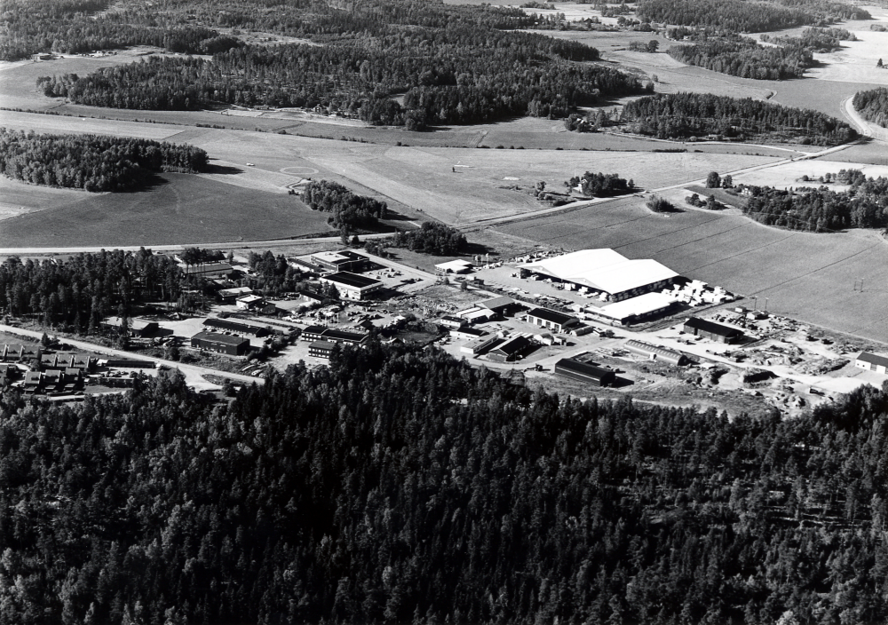 Flygfoto över Rosendals industriområde. Det stora ljusa taket tillhör Cananda bygg AB. Vägen som går genom landskapet är Väsbyvägen