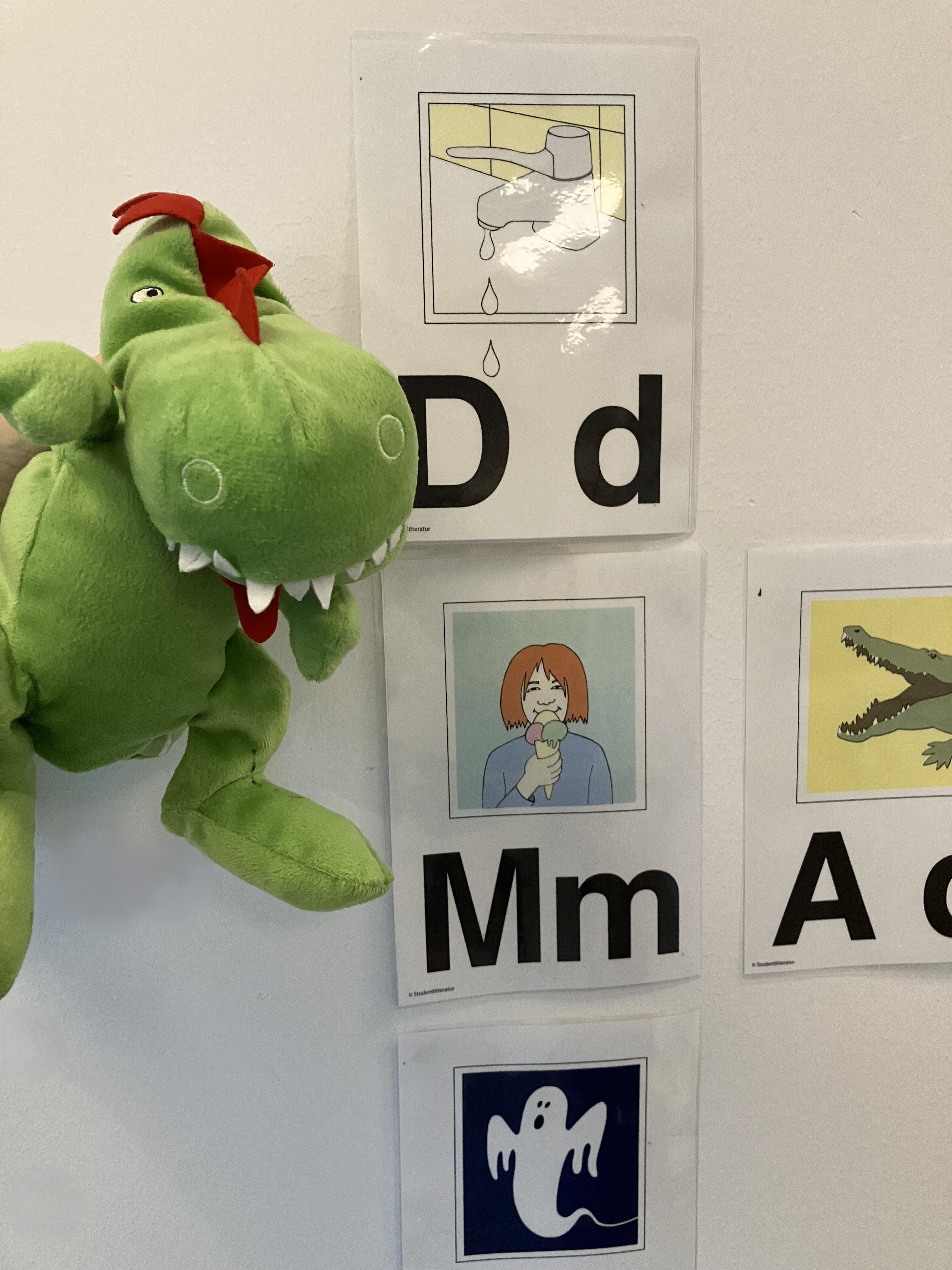 Whiteboardtavla med mjukisdjur i form av en drake och bokstäver tillsammans med bild som ska ska en koppling mellan ord och aktivitet, objekt, annat.
