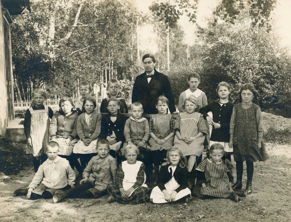 Lärarinnan Anna Gauffin tillsammans med skolbarnen utanför  Gamla missionshuset  på  Olsborgsvägen  Rad 1 nedifrån fr v  Bert Ohlsson   Bengt Andersson   Mary Jansson   Astrid Krieg   Margareta Lindström (Thompson). Rad 2 fr v:  Inga Jansson   Karin Söderberg   Härdis Karlsson   Elsa Glassel   Hugo Nordström   Ingrid Larsson   Märta Andersson   Greta Nygren  och  Alice Lundqvist.  Rad 3:  Evert Pettersson   Ivar Augustsson  och Berta Olsson.