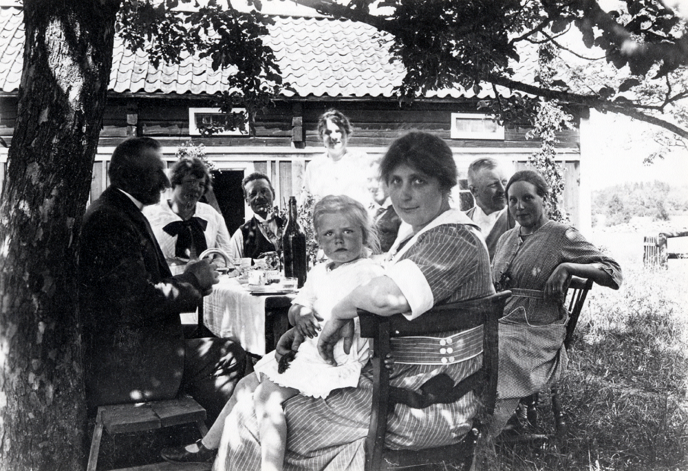 Kaffekalas i gamla gården i Kull.  Runt bordet sitter fr v August Ahlén, Helga Ahlén, Alfred 'Pelle' Lund, okänd,    Helmer Ahlén och hans hustru Anna Ahlén samt Tyra Lund född Ahlén med dottern Elisabeth i knäet