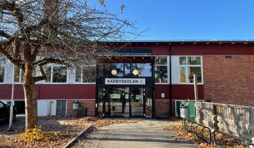 Entrén till skola. Skylten ovanför entrén säger Karbyskolan. Brun tegelbyggnad.