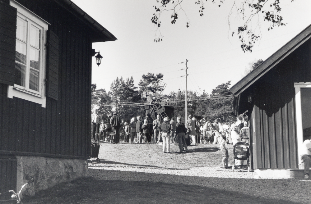 Össeby hembygdsförening firar 30-årsjubileum med sång, servering, musik och dans vid Kvarnstugan, Össeby-Garn.  Mellan husen syns Brottby kvarn.  Kvarnstugan har renoverats och är numera föreningens lokal för program och sammankomster. T v syns ett nyuppfört hus med toalett och redskapsbod