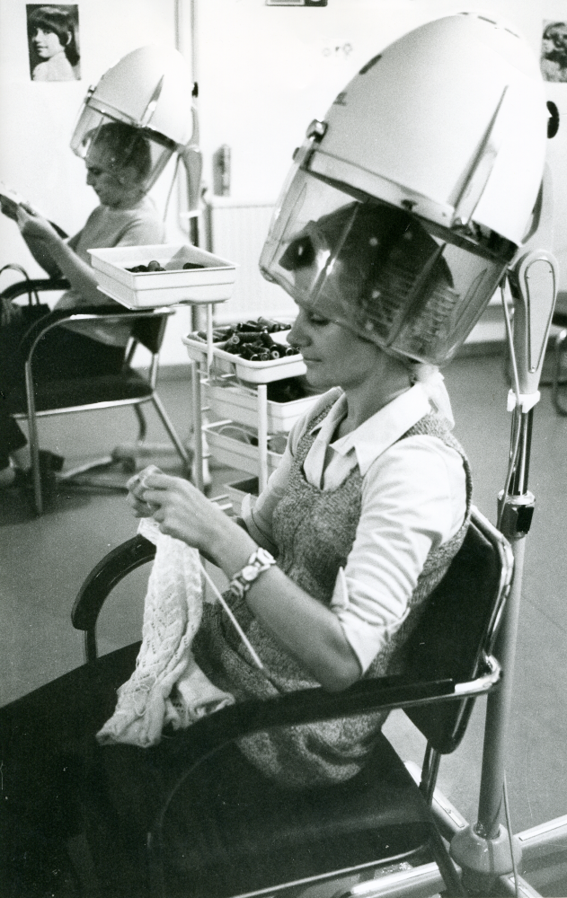 Britt Karlsson, gift med Arne Karlsson, Frösunda handel, avvecklar sin damfrisering. Här sitter salongens sista kunder under varsin torkhuv. Kvinnan närmast i bild sitter och stickar.
•Fotografiet ingår i bildserien ”Vardagsliv i Vallentuna kommun” av Rachael Gough-Azmier & Gunilla Blomé, Haga Studios HB.
