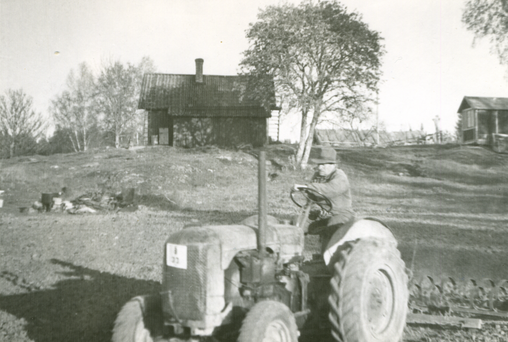 På baksidan av torpet Fagermoda kör torpets ägare Carl-Henrik Andersson sin traktor. Stugan som skymtar till höger i bild var en gammal kolonistuga som man hämtat från Kungsholmen i Stockholm. Original och uppgifter Nolle Andersson, son till Carl-Henrik Andersson.