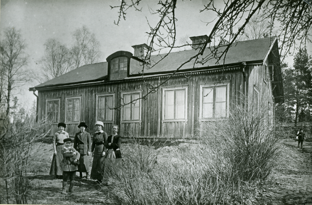 Uppgift vid fotot: Haga Ormsta 1:69. Personerna är ej identifierade. En av de systrar Sjöberg som bodde här förr, Alma, var gift med fjärdingsman Karlsson. Fastighetsbeteckning är Ormsta 1:39. Ursprungligen var huset uppfört på Kusta, men flyttades till sin nuvarande plats ca 1860. Här bodde på den tiden ortens barnmorska och här bildades Vallentunas första frikyrkoförsamling. Uppgift om fotoår saknas, men troligen slutet av 1800-talet eller första delen av 1900-talet. Se även bilder med löpnummer 250, 6017 och 6926.