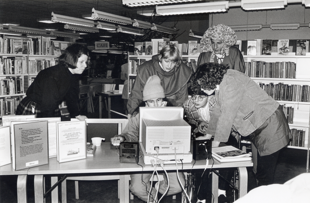 Bokfest 1993 i Vallentuna bibliotek med gycklare från Tellus Hjältar. Årets tema för bokfesten är Rum för kunskap med diverse olika multimedia. Lena Lundgren visar ett dataprogram med bibliotekskunskap anpassat för barn och ungdomar