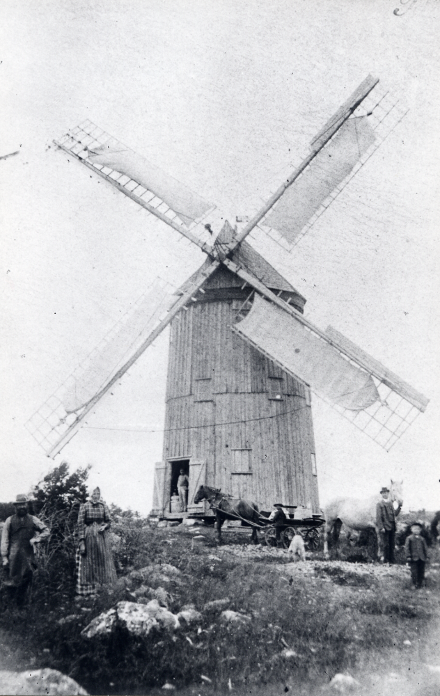 Kvarnen fanns ursprungligen i Sköldnora mellan Täby och Fresta. Kvarnen flyttades ca 1910-15 till Henriksborg i Grana vid infarten till Nähle gård av familjen Henriksson då Algot gifte sig. Algot var mjölnare och snickare och drev Grana kvarn fram till 1926. 1947 monterades kvarnen ner, då den hade förfallit. T v står Johan Henriksson och Klara Henriksson, Algots mor och far. I dörren står mjölnare Algot Henriksson och pojken t h är Algots son Holger Henriksson. Mannen med hästen är Albert Jansson från Mellangården i Nähle. Han födde upp skimmelhästar. Denna häst heter troligen Sally. På kärran ev Melker Jansson. Publicerad i DN runt stan 1987-03-19. Svar från Karin Hallongren född Henriksson och tre svar från Torsten Berggren i Täby.