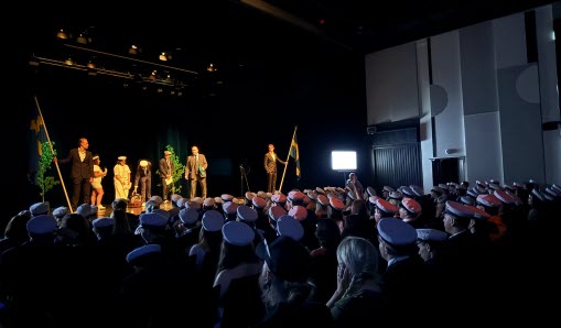 Alla studenter sittandes i bänkraderna på teatern med vita mössor, på scenen svenska flaggor och talhållare
