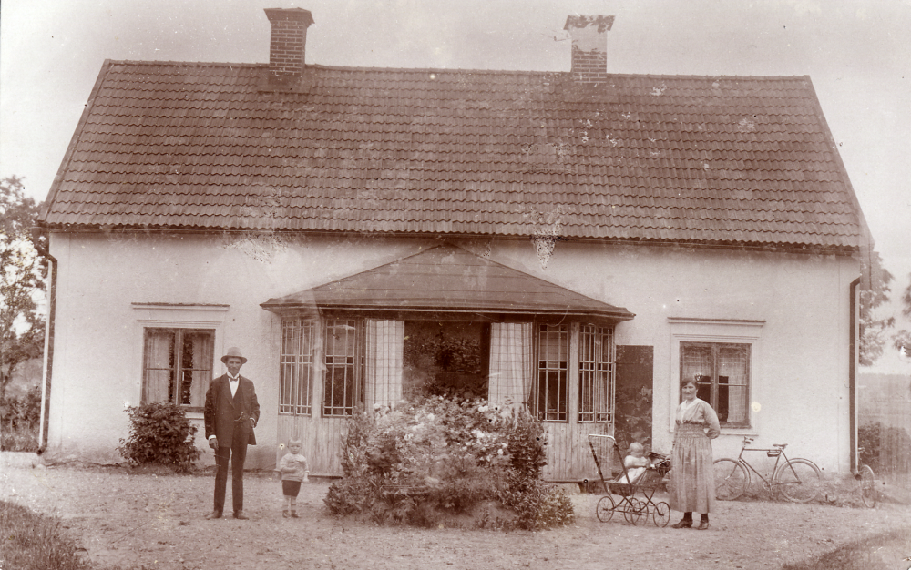 På gårdsplanen framför Torsholma gård i Frösunda står gårdens ägare Ernst Jansson med sin son Gustaf, född 1917.  T h står hustrun Anna med dottern Anne-Marie i barnvagnen.  1937 antog Gustaf namnet Thorsaeus.  Vid huset högra gavel står en cykel som Ernst använde när han cyklade till Finsta för att fria till Anna