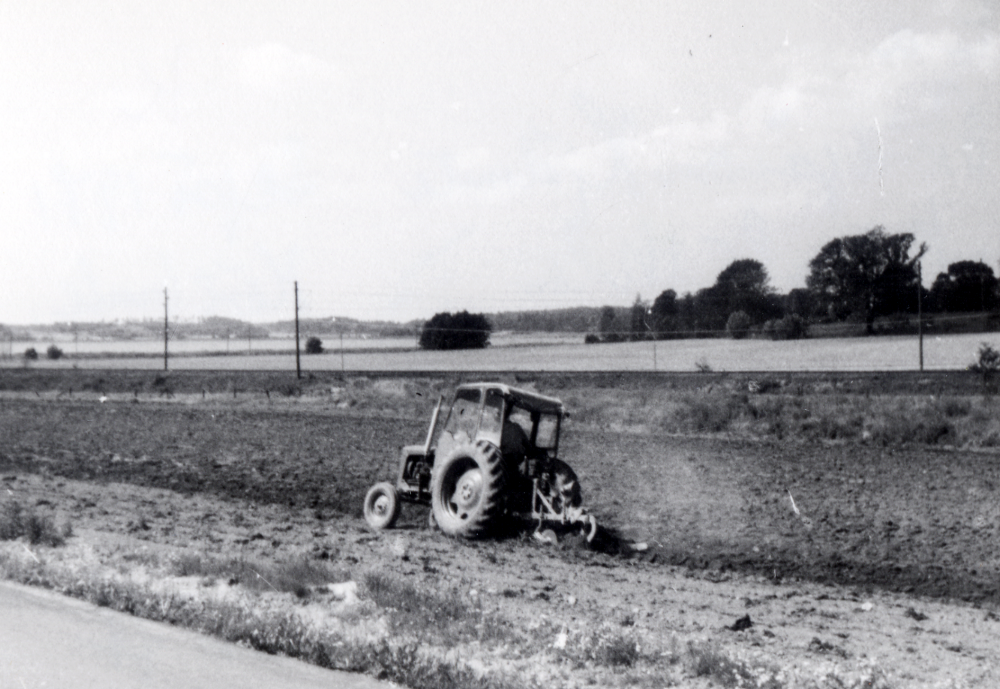 Höstplöjning på mark som tillhör Vallentuna prästgård nedanför Hjälmstavägen med traktor. I bakgrunden skymtar Vallentunasjön