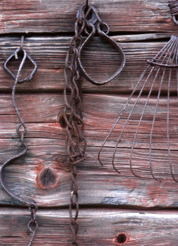 Rostiga redskap och kedjor vid torpet Ängsberga. Det som hänger i mitten användes till att tjudra fast en häst. Torpet Ängsberga hade 17 hektar och 5 dagsverken till Lingsberg. Fotografiet ingår i bildserien Några torp i Vallentuna 1970 som köptes av Vallentuna kommun. Dokumentationen gjordes mot bakgrund av den snabba förvandling av kulturlandskapet som skett och ännu sker. Många torp anlades under den svenska landsbygdens folkökning under slutet av 1700-talet och decennierna framöver. Dessa torp och små gårdar försvinner alltmer då de inte längre är lönsamma. Kulturmiljö.