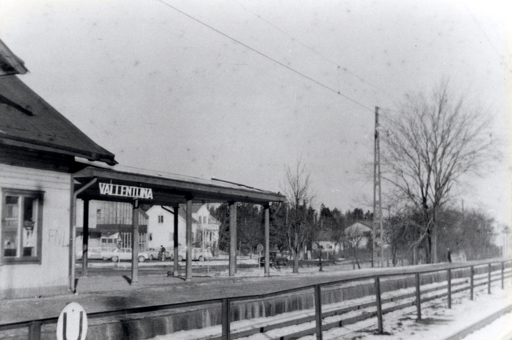 Vallentuna järnvägsstation.  Järnvägsrestaurangen "Flugan" har brunnit ner norr om stationshuset.  Under taket som tidigare förband de två byggnaderna ser man västra gaveln av Konsumhuset (nuvarande Torghuset) samt Villa Nysäter med adress Banvägen