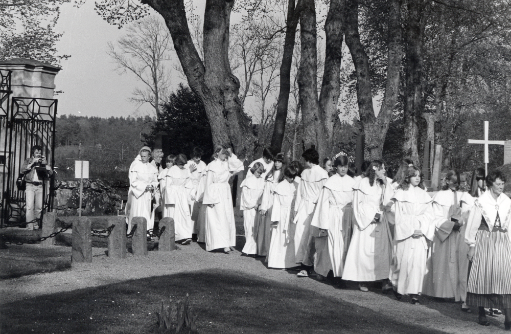 Konfirmation i Vallentuna kyrka.  Konfirmander tågar från Klockargården genom grinden in till kyrkan.  Längst fram går Els-Marie Carlegrim