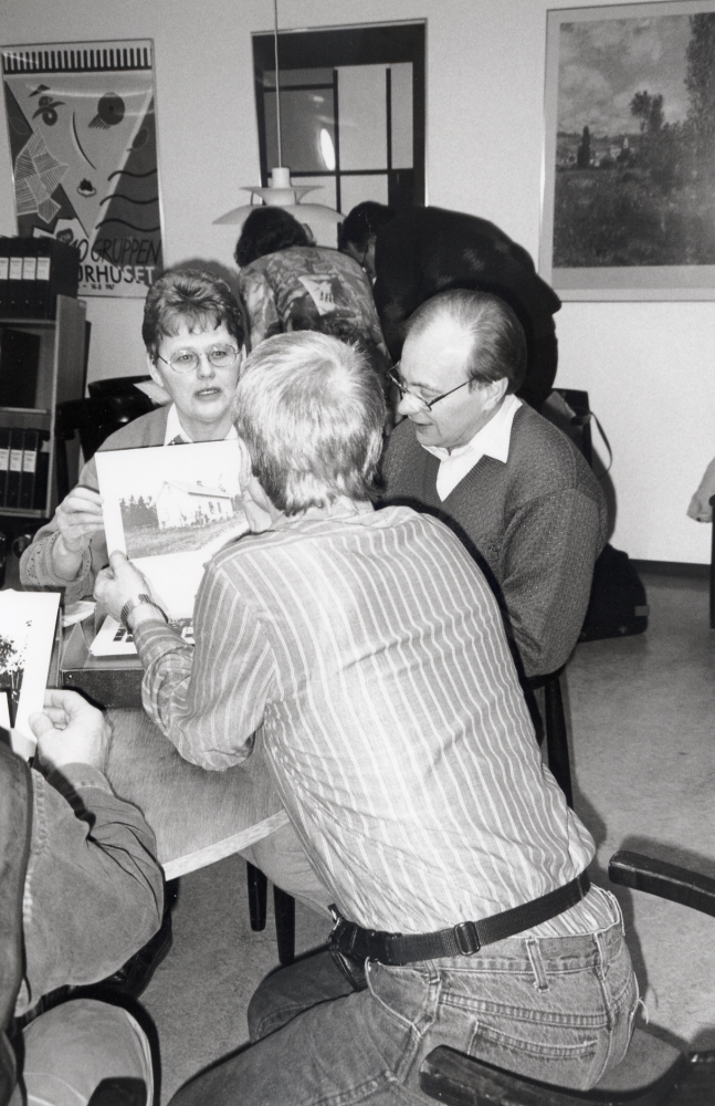 På initiativ av Elisabeth Feldt besöker några av f d medlemmar i Össeby Spisarklubb Vallentuna bildarkiv vid en återträff.  Övriga deltagare har växt upp i Össeby-trakten.  Man samlas kring en enkel måltid i bibliotekets lunchrum.  Sedan tittar och minns man bland arkivets fotografier.    Vid bordet i bakgrunden står Inger Uddén och Lasse Jansson.  Sittande fr v Agneta Lundh, bredvid henne Tony Lundh.  Med ryggen mot kameran Gerth-Åge Frisk