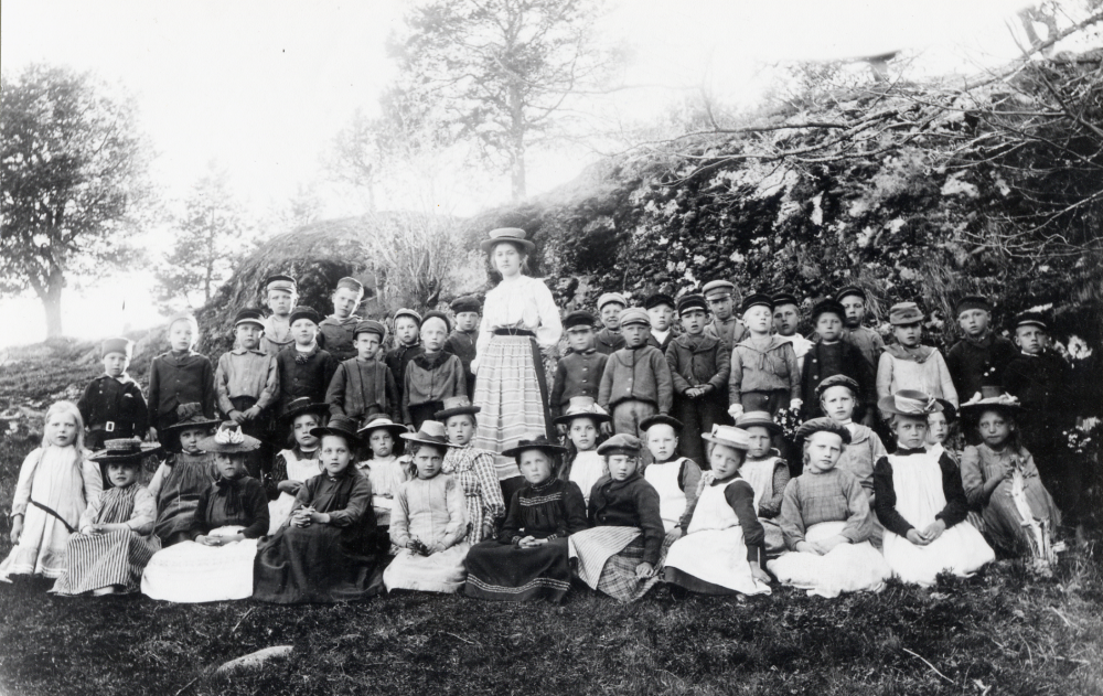 Lärarinnan  Nanny Skoglund  tillsammans med skolbarnen utanför  Össeby-Garns kyrkskola. Andra raden sittande nr 3 fr v: Anna Kjellström, gift Forsberg, frånToftesta gård