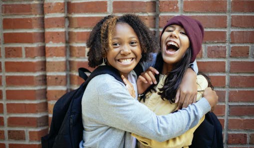 två tjejer står utanför skola och skrattar tillsammans