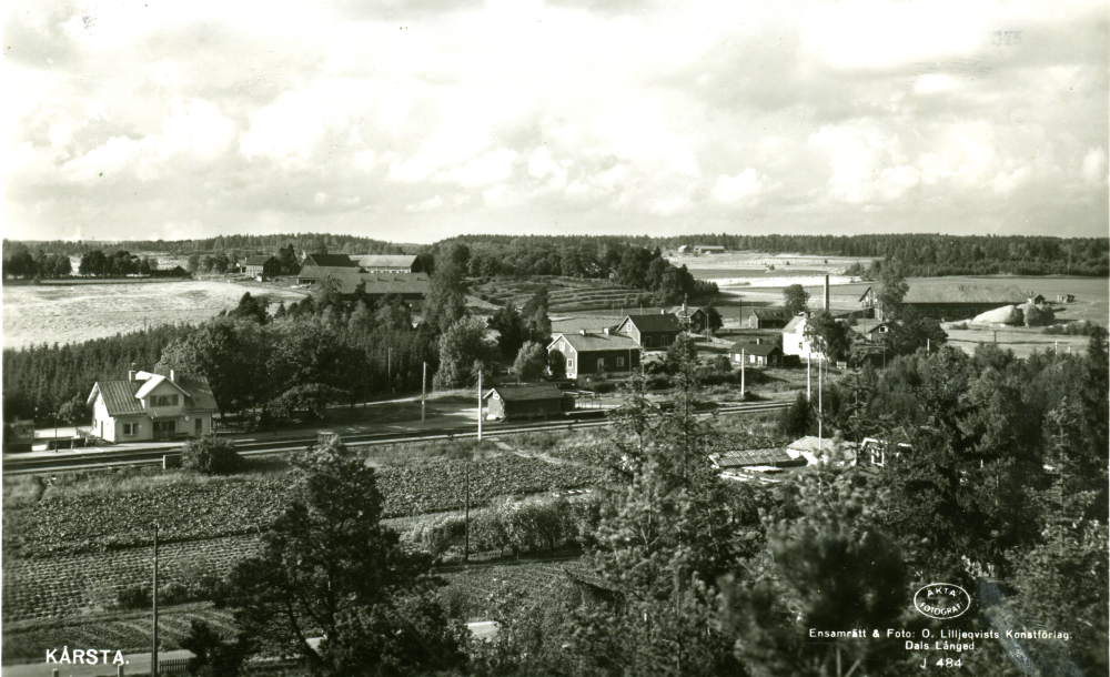 Vy över Kårsta med Kårsta järnvägsstation t v,  i  bakgrunden syns Backa gårds ekonomibyggnader. I förgrunden syns Åke Edlinds rabarberodling vid Eriksdal.

Uppgift om fotoår saknas.