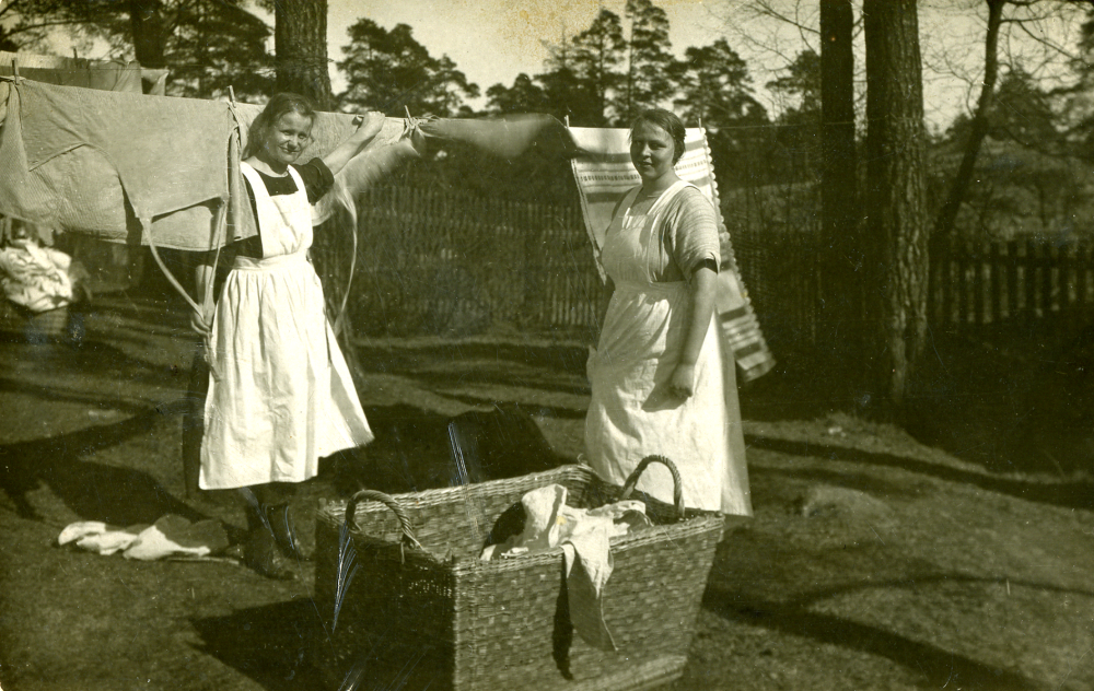 Rosa Karlsson och väninnan Emmy? hänger tvätt på Lovö tvättinrättning.  Rosa cyklade fram och tillbaka från Össeby-Garn till Lovön.  Hon gifte sig 1934 med Ruben Johansson och de  brukade jorden tillsammans på Garns Gillberga, söder om Össeby-Garns kyrka. Rosa var dotter till en statare som bodde på Nybygget vid Husa gård, dessförinnan hade Rosa familj flyttat praktiskt taget varje år