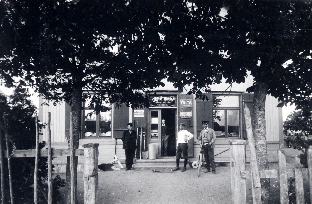 O E Mattssons handelsaffär även kallad  Frösunda handel.  T v framför ingången står  Johan Andersson  extra banvakt vid Roslagsbanan. T h står en man med en  cykel.  Läs mer i Lanthandlare i vallentunasocknarna vid Roslagsbanan