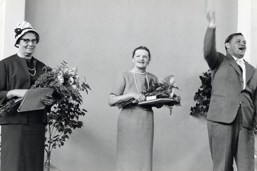 Lärarinnorna  Margit Oppermann  t v och  Edit Lindström  avtackas med blommoroch leverop av skolstyrelsens och kommunfullmäktiges ordförande  Bertil Tillborg  i  Hjälmstaskolans aula  ??                            När de går i pension????