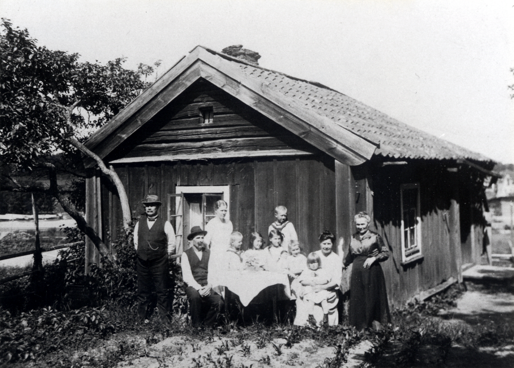 Backstugan Kosveden i Kårsta troligen midsommarafton 1923.  Stugan låg ca 600 m söder om Backa gård och revs 1937.  Fr v står August Magnusson, Axel Arvid Magnusson, Jenny Rödin, gossen Erik Rödin, flickorna Irma och Iris Magnusson, stående gossen Tage Rödin, flickan Ingrid Magnusson, Hilma Magnusson med fosterflickan Greta Åsell i knäet samt Betty Magnusson