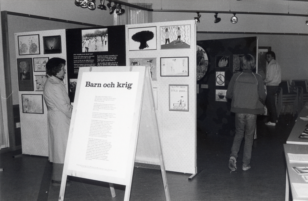 Utställningen Fredsfostran pågick i Vallentunasalen 12 september till 4 oktober 1983 arrenderad av Vallentuna fredförening och Vallentuna kulturnämnd. Pojken t h med ryggen mot kameran heter Magnus Hillbo