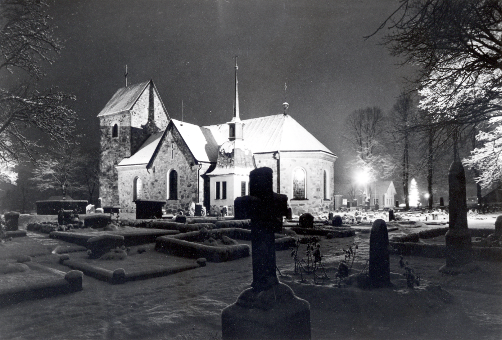 Vallentuna kyrka vintertid i strålkastarbelysning. Foto i broschyr om Vallentuna 1970