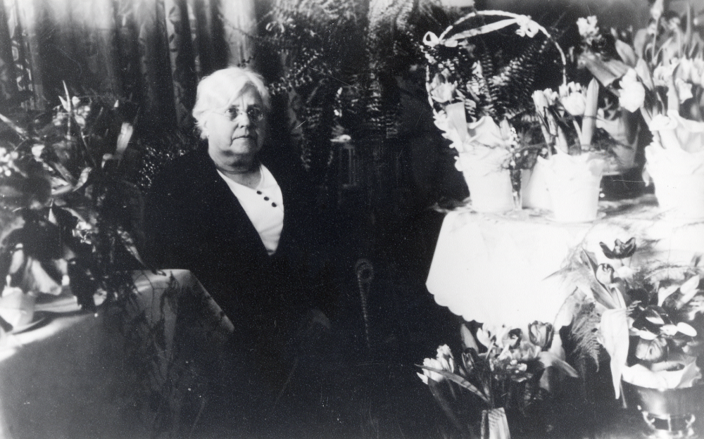 Lärarinnan Mathilda Linde tjänstgjorde i kyrkskolan i Össeby-Garn.  Hon fyller 75 år den  13 februari 1934 och fotograferas med alla blommor