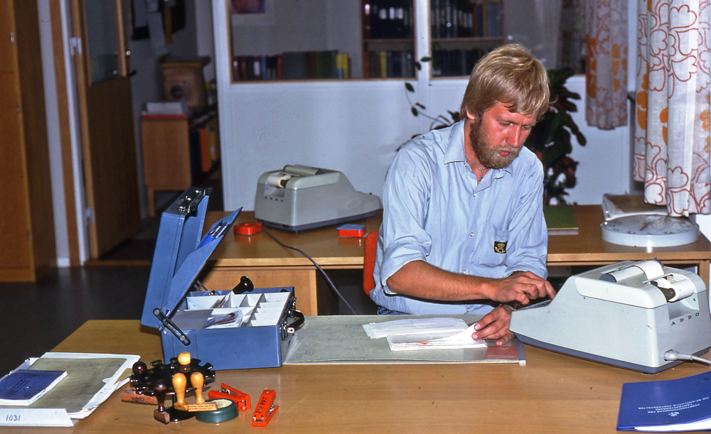 En arbetsdag med lantbrevbärare Mikael Mattsson. Postkontoret på Tuna torg; Postkontoret på Tuna torg där Spel och lek nu (2010) ligger. Mikael Mattsson redovisar kassan ca 17.00-18.00 på kvällen efter dagens lantbrevbärartur. Lantbrevbärarna brukade ha med sig ca 40 pensioner om dagen och tog emot ca 40 inbetalningar om dagen. De lämnade även och tog emot paket på sina turer. Rummet som syns i bakgrunden är postmästarens Olle Olssons rum.