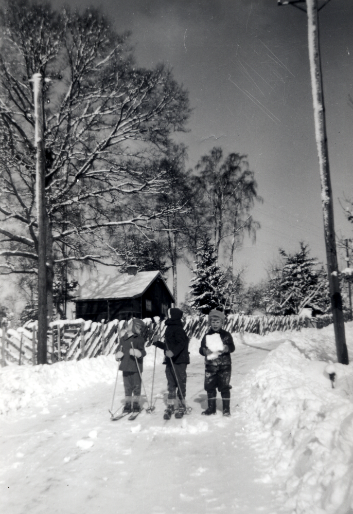 Vinterväg utanför sommarstugan Hasselbacken vid Wasavägen, Djurgården i Lindholmen.  Stugan ägdes av Eric Holmberg med familj. Barnen, två på skidor fr v Per-Anders Karlsson, Annika Ahlsén och Lars Ståhl med en snökoka i famnen