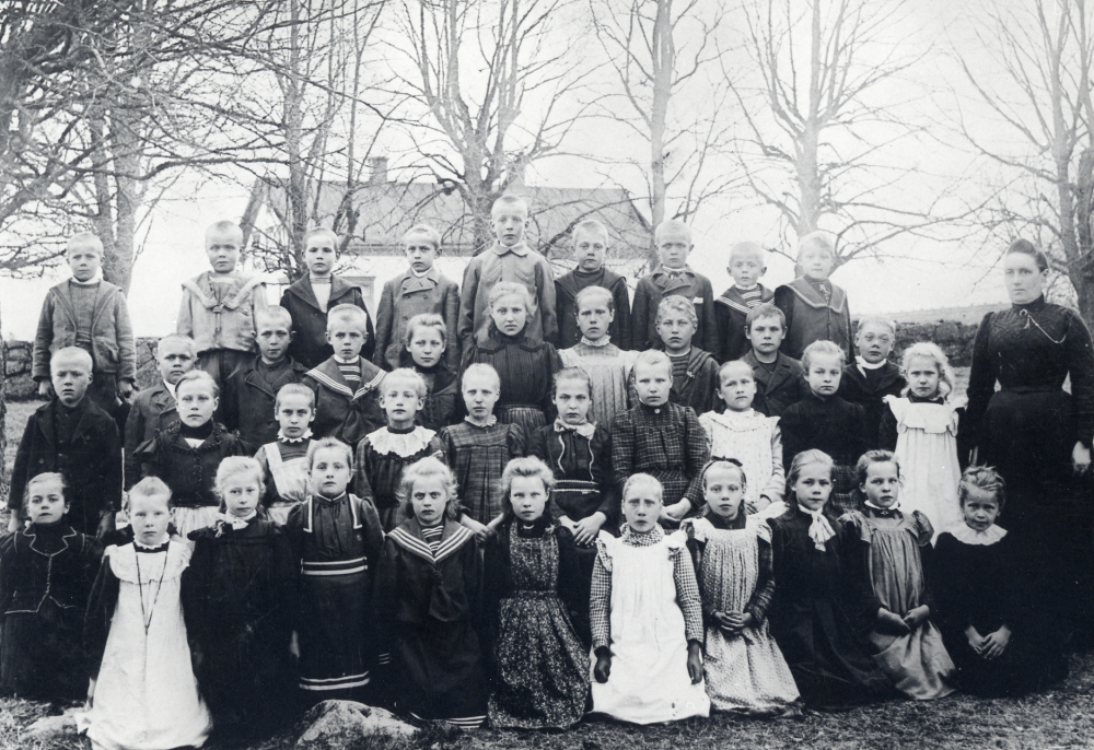 Lärarinnan Hanna Krantz tillsammans med skolbarnen på Vallentuna kyrkogård I bakgrunden syns Klockargården barnens skola. Nr 3 fr v i näst nedersta raden är Anna Johansson, från Oppgården