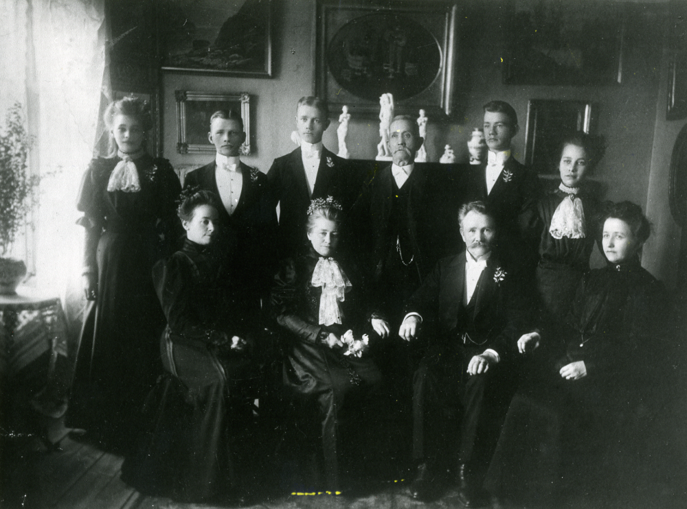Familjebild från familjen Karlsson, bosatt i Lilla Garn.  I övre raden fr v står Elma Karlsson, Fritz Karlsson, Ernst Karlsson, okänd, Emil Karlsson och Ester Karlsson.  Sittande fr v okänd, Emalia Karlsson och bagarmästare Karlsson.  Övriga uppgifter okända.  Alla de yngres namn börjar på E (utom Fritz) liksom Emalia Karlsson, parets barn?  Mannen med skägg och kvinnorna sittande längst t v och t h okända.  Plats och årtal okända
