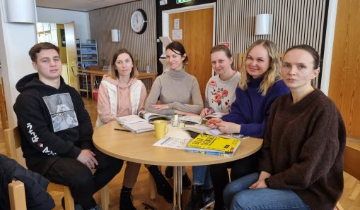 Sex personer sitter vid ett bord med skolundervisningsmaterial på.