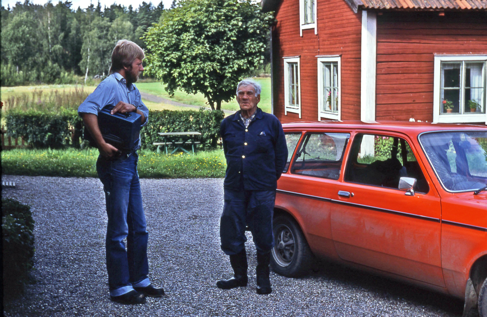 En arbetsdag med lantbrevbärare Mikael Mattsson. Lantbrevbäring i Lappdal;  Lantbrevbärare Mikael Mattson står och pratar med Haldor Bergman på hans gård  i Lappdal. I bakgrunden syns gårdsmuseet. Vägen i bakgrunden går mot Vallentuna åt ena hållet och mot Kusta åt det andra.