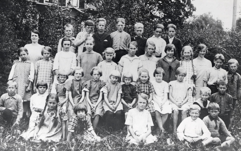 Vid Angars kyrkskola står i övre raden fr v lärarinnan Ida Solem, okänd, Gösta Åkersten Ö Båtmanstorp, Erik Lang, Oskar Jansson Lövlund, Sixten Jansson Lövlund, Olof Eriksson Åsta och Tore Johansson Haga. Rad 2 fr v Rakel Åkersten Ö Båtmanstorp, Ingrid Törnkvist Damsta, Tyra Logren Damsta, Lilly Lindecrantz Rocksta, Gunhild Törnkvist Damsta, Sonja, Gunvor Johansson Rävsta, Inez Eriksson Åsta, Cissi Olsson Åsta, lärarinnan Elna Andersson, Nils Andersson Lundby och okänd. Rad 3 fr v Roland Andersson, Örsta, Hilding Eriksson Åsta, Anna Lisa Åkersten Åsta, Britt Jansson Lövlund, Rut Jansson Lövlund, Eva Törnkvist Damsta, okänd, okänd, Anna Brita Karlsson Lundhem och okänd. Nedersta raden sittande i gräset fr v Inga Lisa Eriksson Örsta, Herta Åkersten Ö Båtmanstorp, Ingrid Johansson Rävsta, Lennart Olsson Åsta, okänd, Harry Johansson Rävsta och okänd
