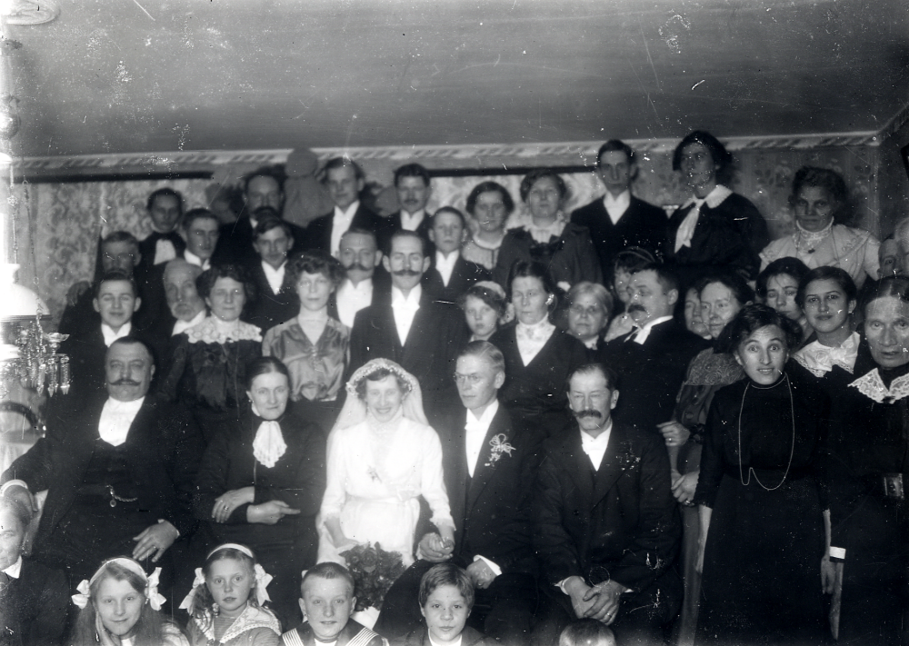 Bröllop mellan Linnea Pettersson och Georg Norberg på 5 december 1914 i Granby gård, Össeby-Garn. Längst ner t v okänd, Märta Johansson Granby, Lisa Gustafsson Åttesta, Bertil Johansson Granby, okänd, okänd. Sittande längst ner fr v åkare Johansson Granby, Amanda Pettersson brudens mor Granby, bruden Linnéa, brudgummen Georg, Albert Pettersson brudens far. Stående rad 2 fr v Axel Johansson Stockholm, okänd, Ester Nilsson, Valborg Lidén, Emil Nilsson, Oscar Lidén, ev Linnéas kusin Hilma Johansson, Jenny Norberg brudgummens mor, okänd, ev Märta?, kyrkoherden, okänd, kyrkoherdens fru, okänd Edvina Fröman Skräfsta, Gertrud Johansson och okänd. Översta raden fr v Helmer Gustafsson brudens morbror, Julia Gustafsson Helmers fru, Birger Regny brudens bror, Edvard Regny brudens andra bror, okänd, Ernst Klerke brudens kusin, Ernst Fröman Skräfsta, Gotthold Norberg brudgummens bror, Mia Eriksson Carlsborg Ö-G, åkare Johanssons fru, Helge Eriksson Mias bror, okänd, okänd, okänd och okänd