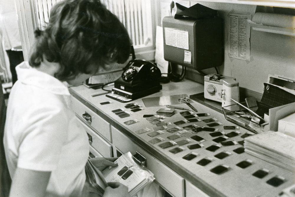 Arbetsplats för tandsköterskan mellan de båda tandläkarnas arbetsrum vid tandläkarmottagningen på Centralvägen 8. Röntgenplåtarna granskas av tandsköterskan.
•Fotografiet ingår i bildserien ”Vardagsliv i Vallentuna kommun” av Rachael Gough-Azmier & Gunilla Blomé, Haga Studios HB.