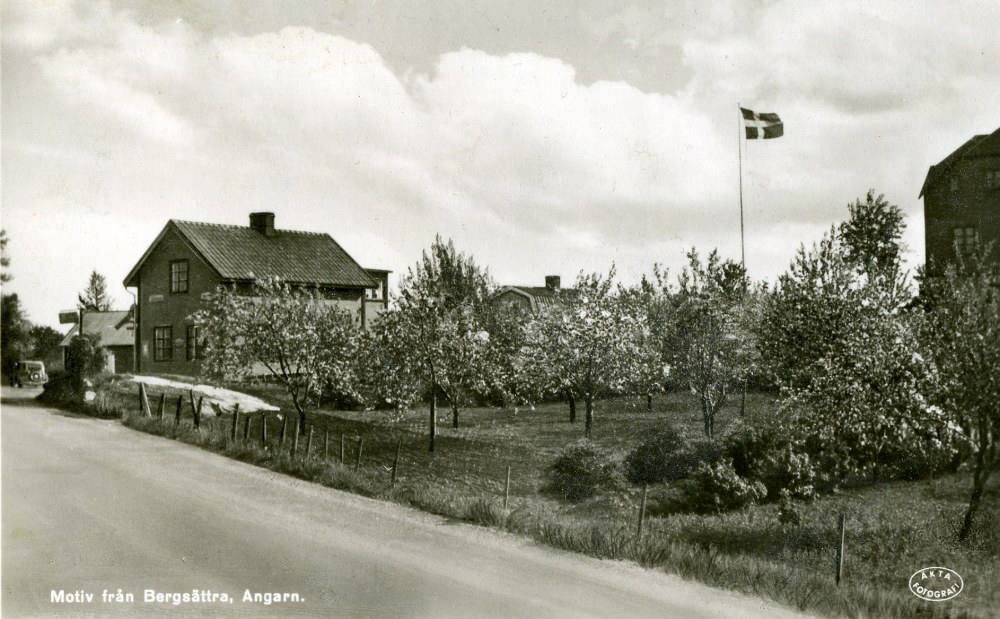 Bergsättra i Angarn sett från norr före 1947 då kaféet byggdes om.  Husen finns vid Gamla Norrtäljevägen i korsningen mot Vallentuna vid Angarns kyrka.  Det ljusa huset som man skymtar taket av, byggdes för Olga Axén som var arbetade som hjälpreda i kaféet, hon dog 1951. Olga hade ett rum och kök i övervåningen.  På bottenplanet var en cykelverkstad, tvättstuga, källare, vedbod och utedass. Seth och Ruth Axén bodde i Axelsberg (utanför bild t h). De drev kaféet  inrymt i det stora huset i bildens mitt, de började med en kiosk på 1930-talet.  Man sålde också Shell bensin, se skylten vid bilen som är en Ford Eifel. Innan Nya Norrtäljevägen byggdes passerade all trafik till och från Norrtälje och Stockholm utanför kaféet