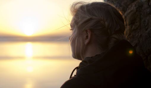 Flicka som tittar på solnedgången över havet