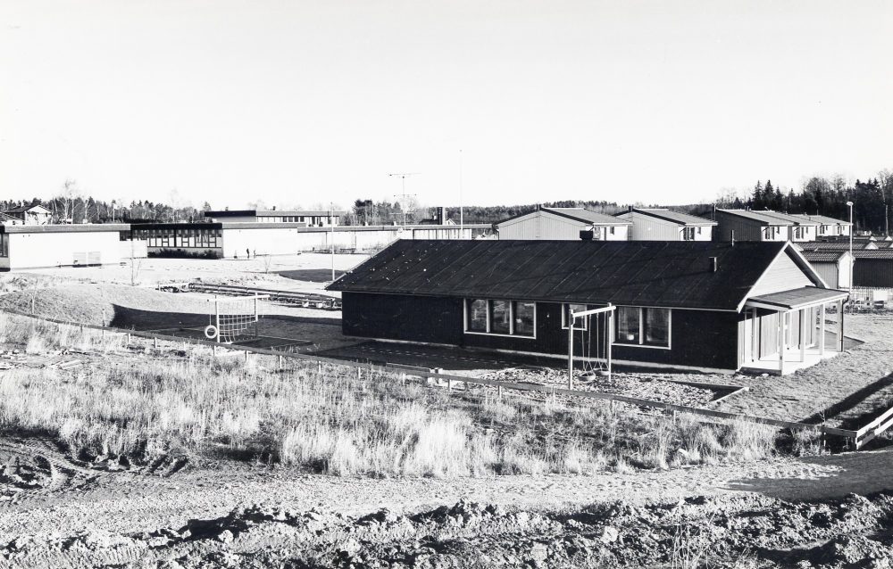 Lindholmens daghem med det nya bostadsområdet Skärholmen i bakgrunden över daghemmets tak. Den vita låga byggnaden längst upp t v är Gusta Vasaskolan. Bostadsområdet har fått sitt namn p g a alla husen är målade i olika skära nyanser