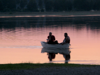 Två personer sitter i en båt i Vallentunasjön vid Kyrkviken i solnedgång.