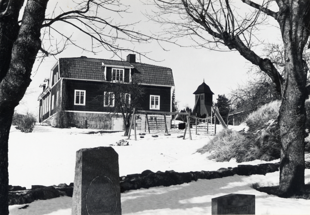 Kårsta kyrkskola  T h om skolan syns  klockstapeln  och i förgrunden gravstenar på  Kårsta kyrkogård