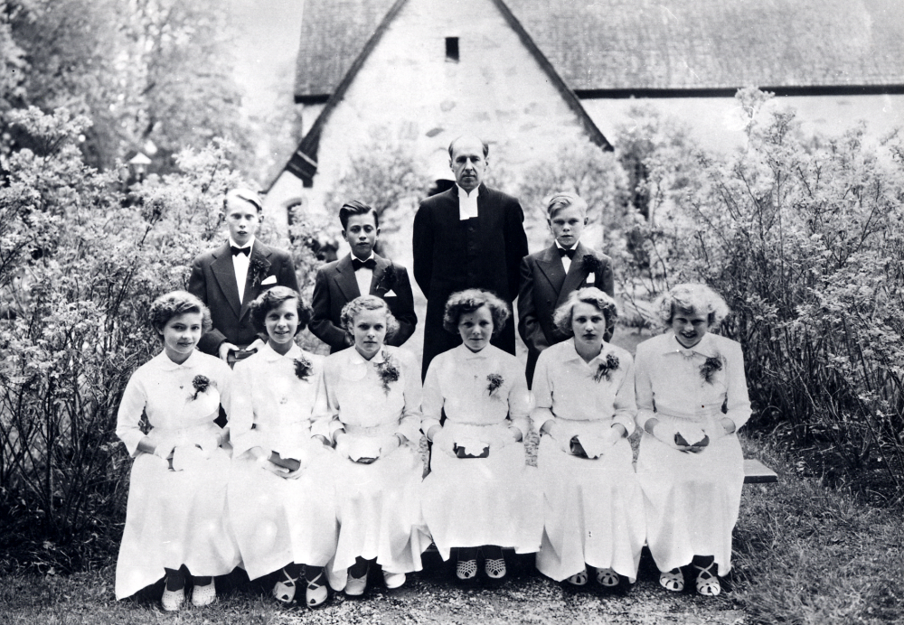 Konfirmation i Frösunda kyrka. Prästen Ture Nilsson tillsammans med konfirmander utanför kyrkan. Nedre raden fr v: Inga Helgöstam Helgö gift Jansson, Maud Jansson Gribbylund, Siv Pettersson Gribbylund, Irene Jansson Karlberg gift Wredh, Siv Nilsson Bygget, Birgitta Berglund. Övre raden fr v Bo Lundin, Arne Stolpe Rolsta och Rolf Arne Jansson Rolsta
