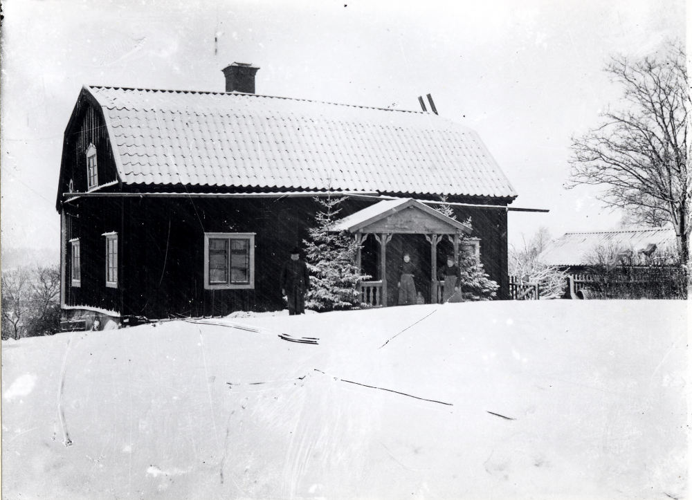 Abraham Gustavsson och hans hustru Sofia Gustavsson, Algot Laurells föräldrar står framför Åttesta gård tillsammans med en piga som arbetade på gården. Boningshuset är nu rivet